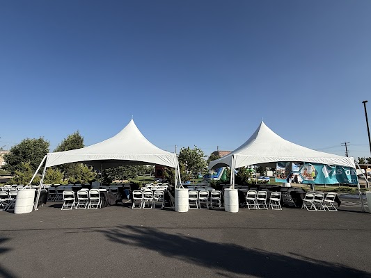 Two white high-peak tents with tables and folding chairs on a paved outdoor event site